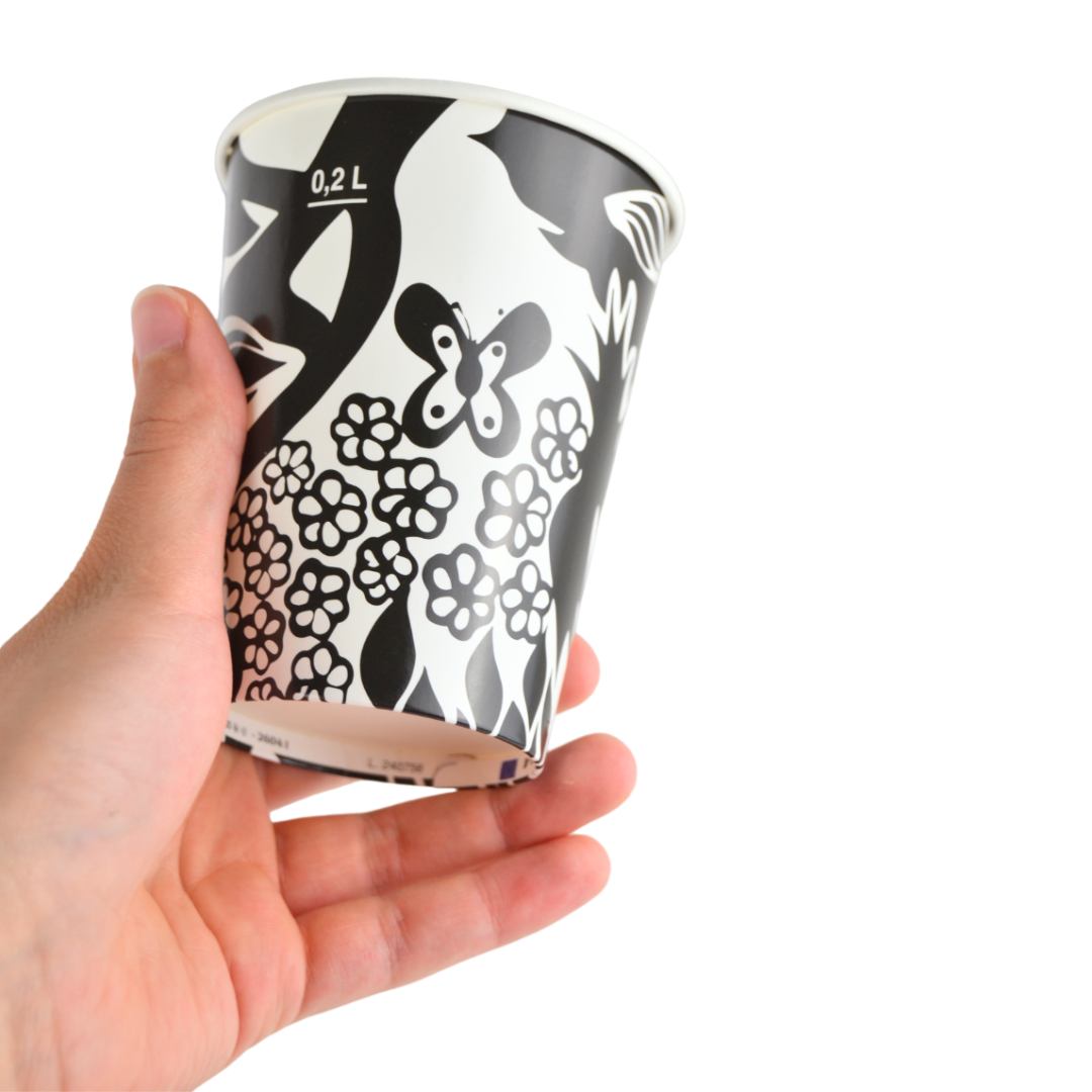 Dettaglio di una mano che tiene il bicchiere in carta nera con decorazione astratta.