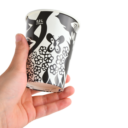 Dettaglio di una mano che tiene il bicchiere in carta nera con decorazione astratta.